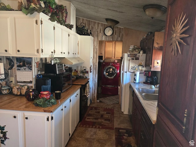 kitchen with wood walls, a sink, freestanding refrigerator, white cabinets, and washing machine and dryer
