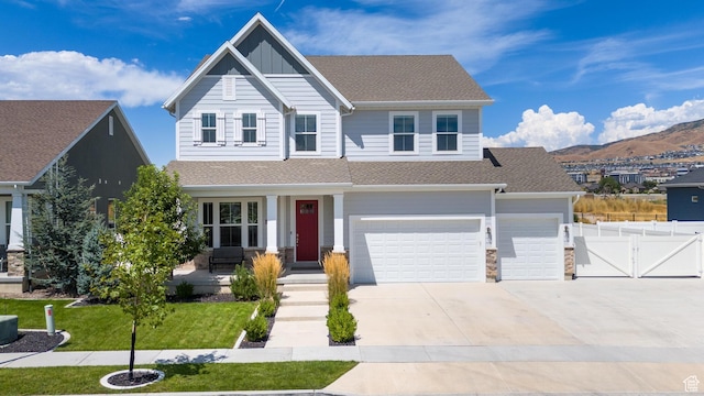 view of front facade with fence, concrete driveway, a front lawn, board and batten siding, and a mountain view
