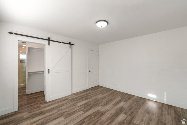 unfurnished bedroom with a spacious closet, baseboards, a barn door, a closet, and wood finished floors