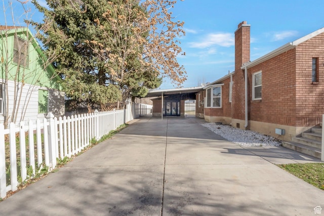 view of side of property featuring fence, a chimney, concrete driveway, brick siding, and a carport