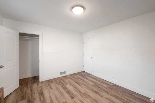 unfurnished bedroom featuring wood finished floors, a closet, baseboards, and visible vents