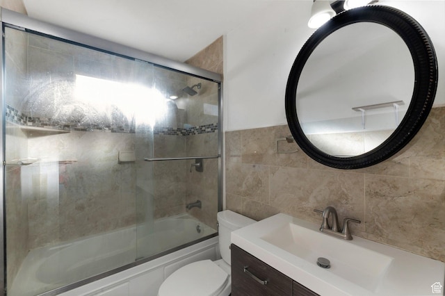 full bathroom with tile walls, combined bath / shower with glass door, toilet, and vanity