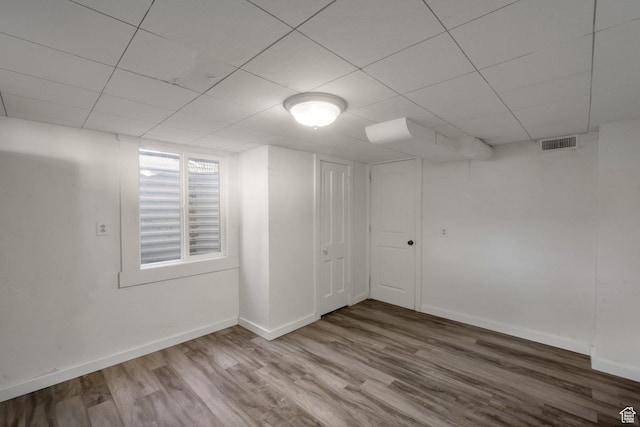 below grade area featuring baseboards, visible vents, wood finished floors, and a drop ceiling