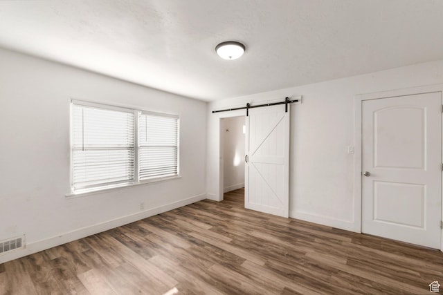 unfurnished bedroom featuring wood finished floors, baseboards, a barn door, and visible vents