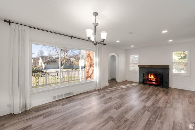 unfurnished living room featuring a fireplace with flush hearth, visible vents, a chandelier, wood finished floors, and arched walkways