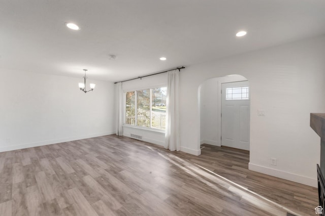 interior space featuring wood finished floors, a chandelier, arched walkways, and a healthy amount of sunlight