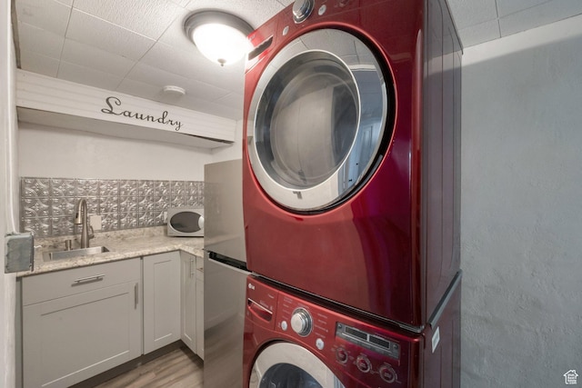 laundry room with stacked washer and clothes dryer, laundry area, a sink, light wood-type flooring, and a textured wall