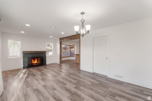 unfurnished living room with a warm lit fireplace, visible vents, recessed lighting, light wood-type flooring, and a notable chandelier