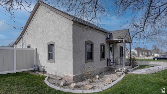view of side of property featuring stucco siding, fence, and a yard