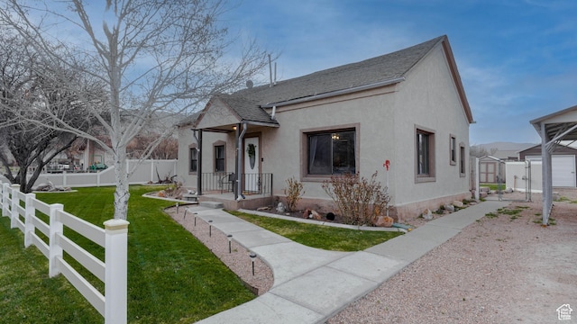view of front of house featuring stucco siding, an outbuilding, a storage shed, a front lawn, and a fenced backyard