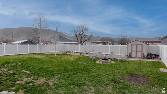 view of yard featuring an outdoor structure, a fenced backyard, a storage unit, a mountain view, and a fire pit