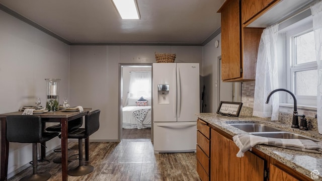 kitchen featuring brown cabinetry, white fridge with ice dispenser, and ornamental molding
