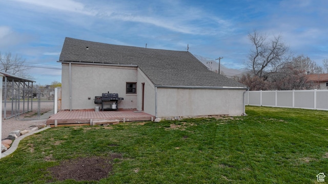 back of house featuring stucco siding, roof with shingles, a wooden deck, a fenced backyard, and a yard