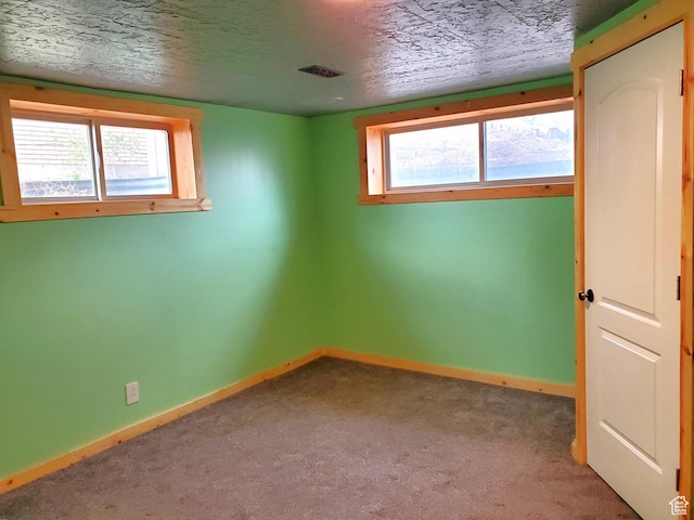 carpeted empty room with a textured ceiling, visible vents, baseboards, and a healthy amount of sunlight