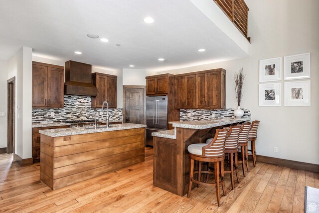 853 W Benjamin Pl, Kamas, UT 84036 - kitchen featuring decorative backsplash, stainless steel appliances, light wood finished floors, a sink, and wall chimney exhaust hood