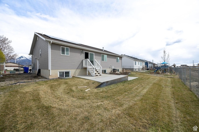 rear view of house featuring a patio area, a playground, a fenced backyard, roof mounted solar panels, and a yard