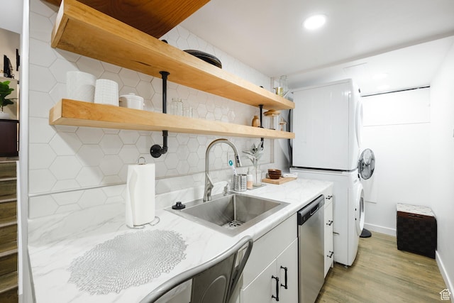 washroom with laundry area, light wood-type flooring, a sink, baseboards, and stacked washer / drying machine