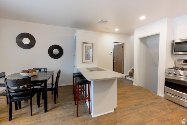kitchen with light countertops, white cabinets, light wood-style floors, a breakfast bar area, and appliances with stainless steel finishes
