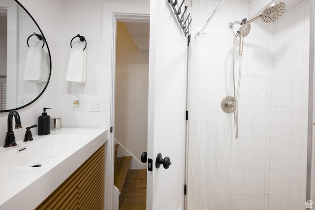 full bath with tiled shower, vanity, and wood finished floors