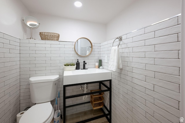 bathroom featuring toilet, a sink, and tile walls