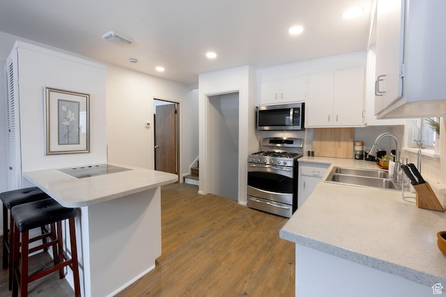 kitchen featuring appliances with stainless steel finishes, wood finished floors, light countertops, a sink, and a breakfast bar area