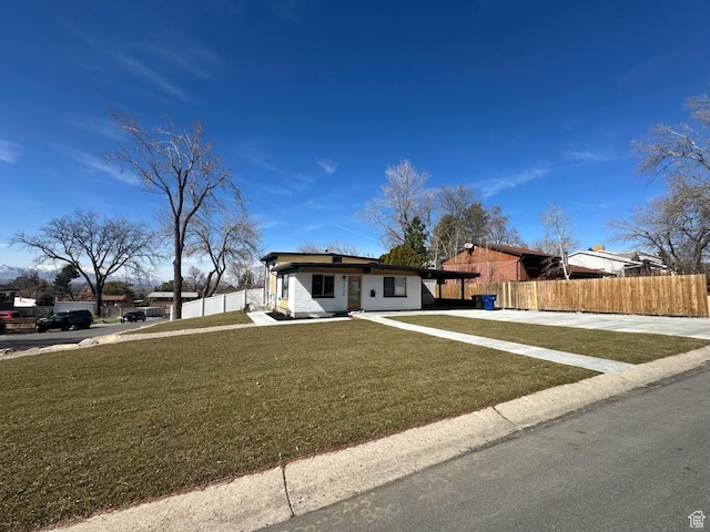 view of front facade featuring concrete driveway, fence, and a front lawn