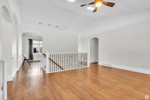 empty room with visible vents, light wood finished floors, a ceiling fan, arched walkways, and vaulted ceiling