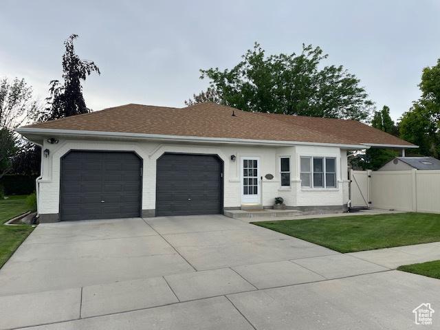 ranch-style home with fence, an attached garage, concrete driveway, a front yard, and roof with shingles