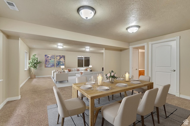 dining room with baseboards, a textured ceiling, visible vents, and light colored carpet