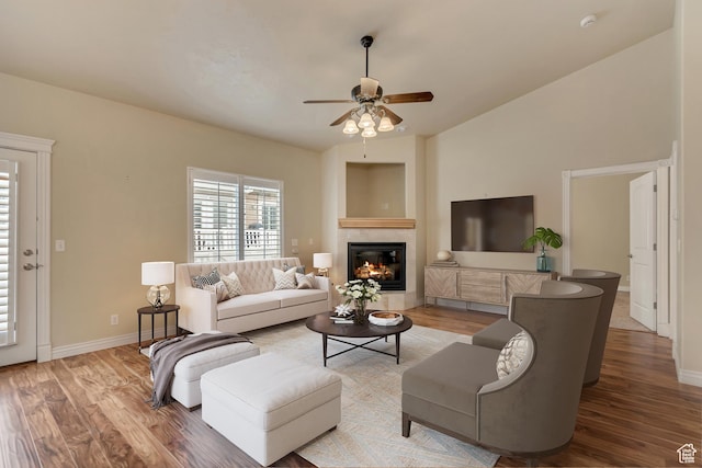living area featuring a ceiling fan, a fireplace, wood finished floors, lofted ceiling, and baseboards