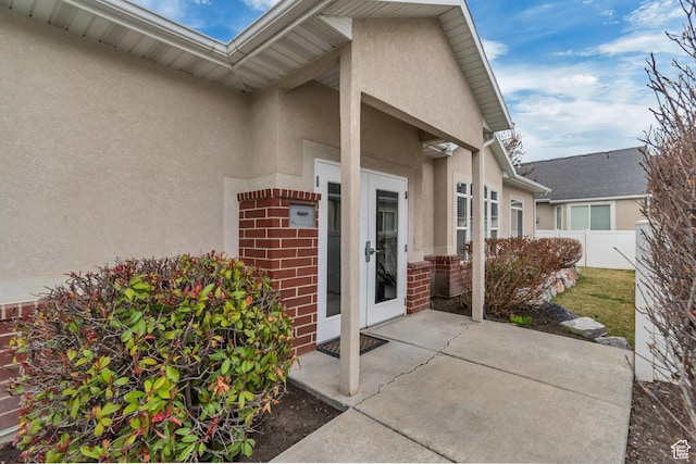 doorway to property with fence, brick siding, stucco siding, french doors, and a patio area