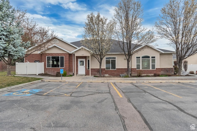 ranch-style home featuring brick siding, uncovered parking, stucco siding, and fence