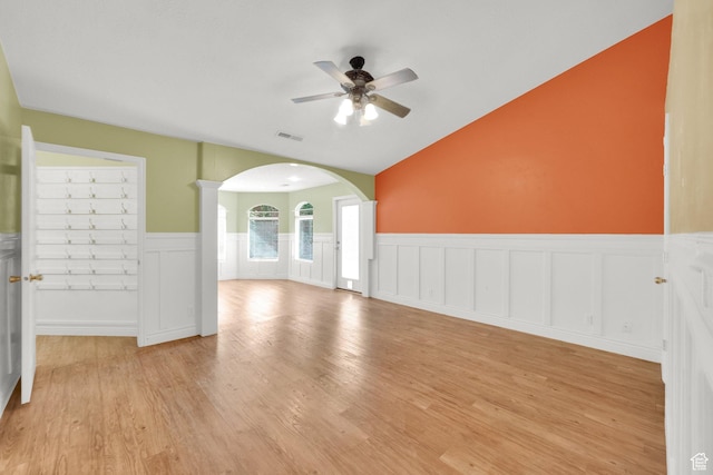 unfurnished living room featuring a ceiling fan, lofted ceiling, light wood-style flooring, visible vents, and arched walkways