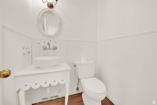 bathroom featuring a wainscoted wall, toilet, wood finished floors, and a sink