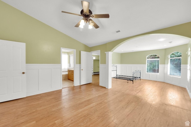 unfurnished living room with a wainscoted wall, arched walkways, light wood-style floors, and ceiling fan