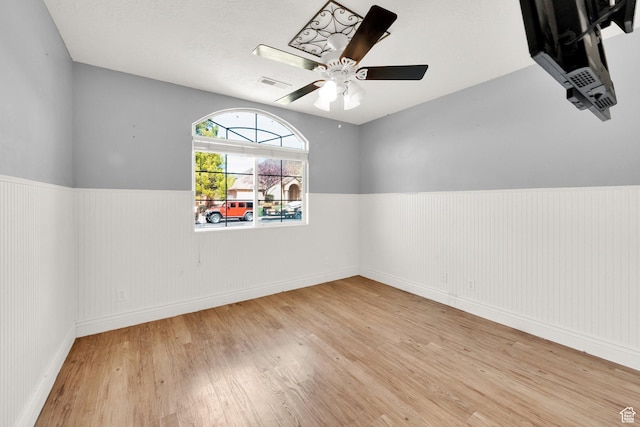 spare room with a ceiling fan, wainscoting, wood finished floors, and visible vents