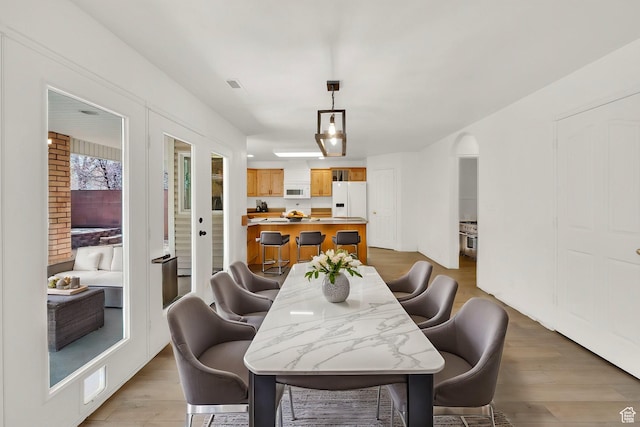 dining room featuring arched walkways, light wood finished floors, and visible vents