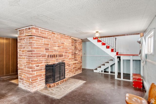 377 E Shore Rd, Saint Charles, ID 83272 - unfurnished living room featuring a brick fireplace, concrete floors, wood walls, and stairway