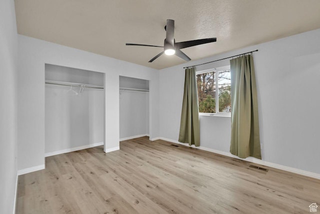 unfurnished bedroom featuring multiple closets, visible vents, baseboards, wood finished floors, and a ceiling fan
