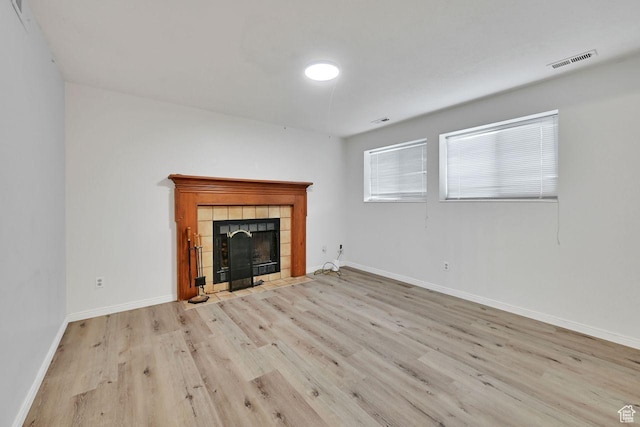 unfurnished living room with a tiled fireplace, visible vents, baseboards, and wood finished floors
