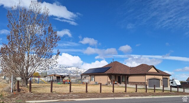 546 S Quirk St, Grantsville, UT 84029 - view of front of house with roof mounted solar panels, playground community, a fenced front yard, and a mountain view