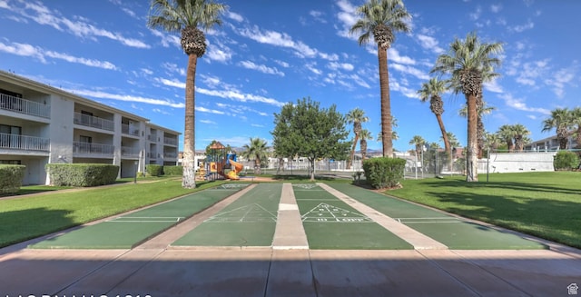 view of community featuring shuffleboard, fence, playground community, and a yard