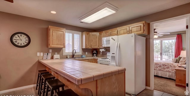 kitchen featuring a breakfast bar area, white appliances, a sink, a peninsula, and light brown cabinets