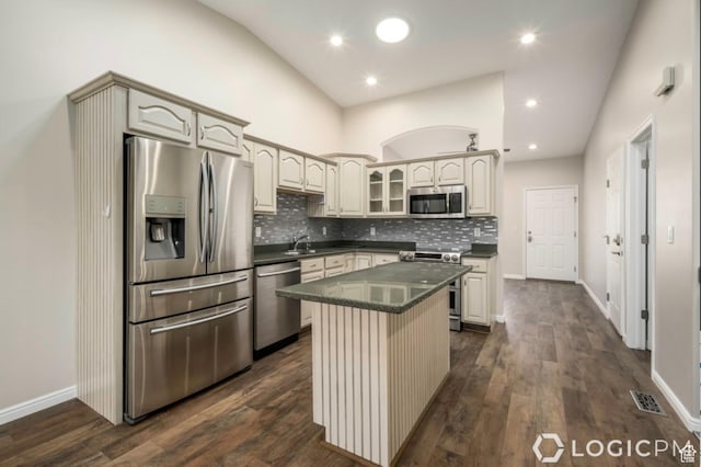 kitchen featuring a center island, glass insert cabinets, dark countertops, tasteful backsplash, and appliances with stainless steel finishes