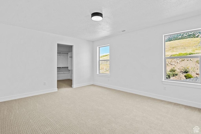 3666 W 2110 S Unit 103, Syracuse, UT 84075 - unfurnished bedroom with a closet, a textured ceiling, baseboards, light carpet, and a walk in closet