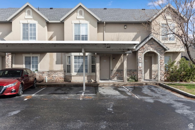 multi unit property featuring stone siding, covered parking, stucco siding, and roof with shingles
