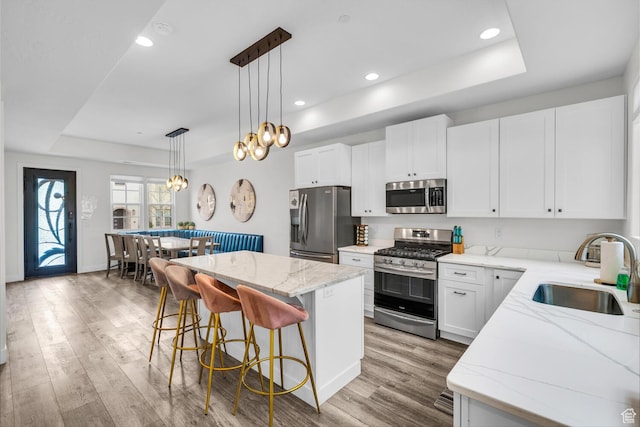 kitchen with a raised ceiling, appliances with stainless steel finishes, a sink, light wood-style floors, and a breakfast bar area