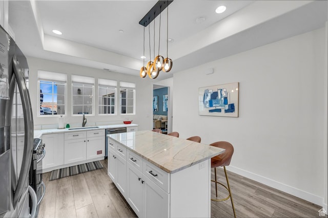 4301 W Canterbury Rd, Hurricane, UT 84737 - kitchen with a tray ceiling, a kitchen island, a kitchen breakfast bar, appliances with stainless steel finishes, and light wood-type flooring