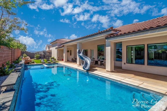 view of swimming pool featuring a fenced backyard, a pool with connected hot tub, a water slide, and a patio area