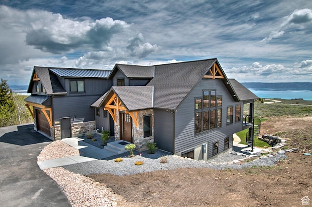 view of front of home with driveway, a water view, a garage, and stone siding